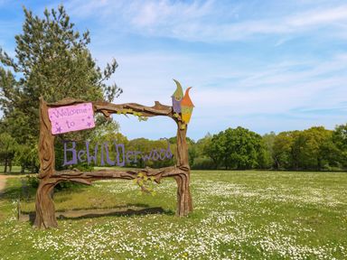 A wooden welcome sign in a field with white flowers and trees in the background at Paws-A-While in Hoveton & Wroxham