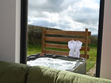 A bubbling outdoor hot tub with two white robes hanging on a wooden fence behind it at Cae Pren in New Mills near Llanfair Caereinion
