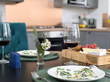 A dining table with plates napkins forks wine glasses flowers and a cheese board in a kitchen at Cae Pren in New Mills near Llanfair Caereinion