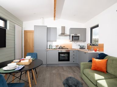 A kitchen and dining area with grey cabinets a green sofa and a black dining table at Cae Pren in New Mills near Llanfair Caereinion