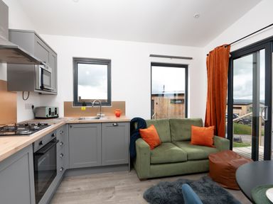 A kitchen with gray cabinets green sofa and orange curtains at Cae Pren in New Mills near Llanfair Caereinion