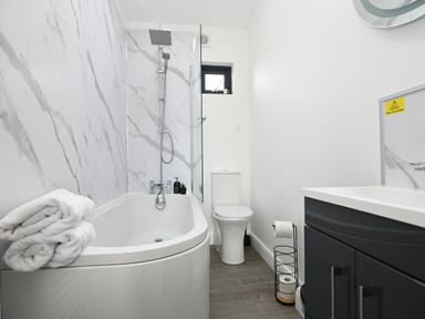 A bathroom with a bathtub shower combination towels on the tub and a toilet next to a sink cabinet at Cae Pren in New Mills near Llanfair Caereinion
