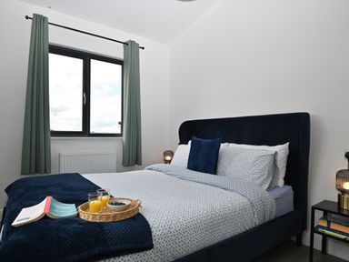 A bedroom with a bed a window with curtains a bedside table with a lamp and books at Cae Pren in New Mills near Llanfair Caereinion