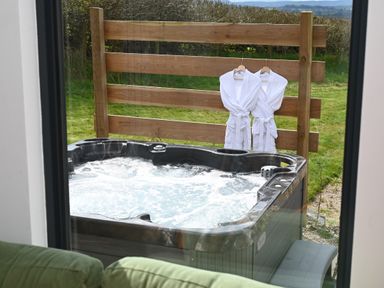 An outdoor hot tub with bubbling water and two white robes hanging on a wooden fence at Cae Pren in New Mills near Llanfair Caereinion