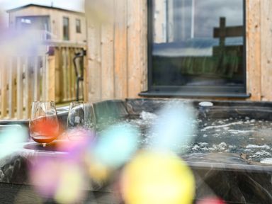 Two glasses on the edge of a hot tub outside a wooden building at Cae Pren in New Mills near Llanfair Caereinion