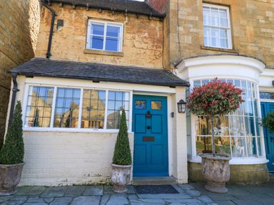 Front of a stone and brick house with blue door and potted plants outside at Broadway Cottage in Broadway