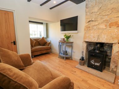 A living room with brown sofas a stone fireplace a wall mounted TV and a window at Broadway Cottage in Broadway