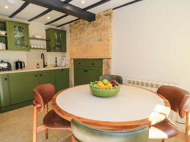 A kitchen with green cabinets a round table with a bowl of fruit and brown chairs at Broadway Cottage in Broadway