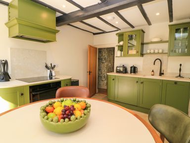 A kitchen with green cabinets a table with a fruit bowl and kitchen utensils at Broadway Cottage in Broadway