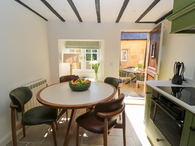 A kitchen dining area with a round table and four chairs and a bowl of fruit on the table at Broadway Cottage in Broadway
