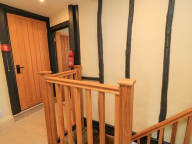 A wooden staircase railing with a closed wooden door and exposed black beams on cream walls at Broadway Cottage in Broadway