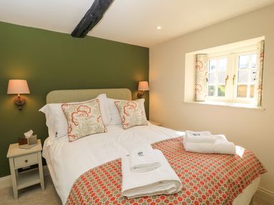 A bedroom with a double bed two bedside tables and a window with patterned curtains at Broadway Cottage in Broadway