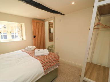 A bedroom with a bed towels on it a wooden door a window and an open wardrobe at Broadway Cottage in Broadway