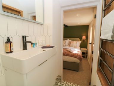 A bathroom sink with soap dispenser and towel leading to a bedroom with a bed and bedside table at Broadway Cottage in Broadway