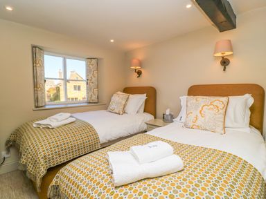 A bedroom with two single beds with patterned throws and pillows by a window at Broadway Cottage in Broadway