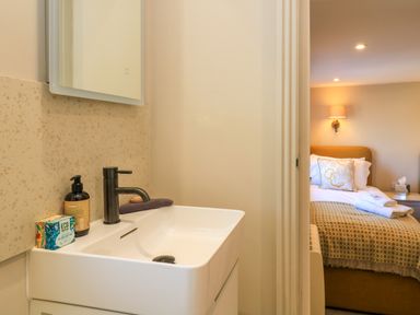 A bathroom sink with soap and lotion next to a bedroom with a bed and bedside lamp at Broadway Cottage in Broadway