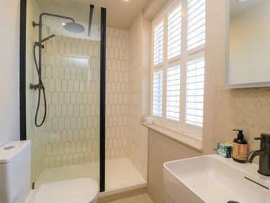 A bathroom with a shower enclosure a toilet a sink with soap and a window with blinds at Broadway Cottage in Broadway