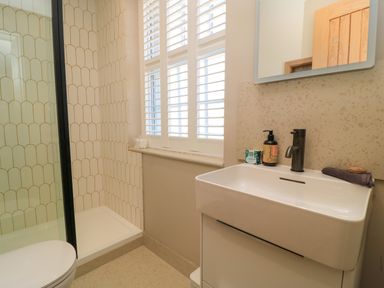 A bathroom with a white sink and black faucet a shower area with tiled walls and a window with shutters at Broadway Cottage in Broadway