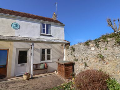 The exterior of a two-story house with a wooden bench near the door and a stone wall beside it at 4 Lymbrook Cottages in Lyme Regis