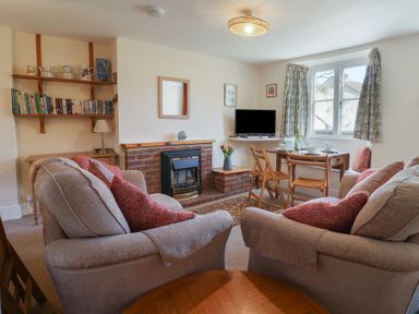 A living room with sofas, a dining table set, a TV, and a fireplace at 4 Lymbrook Cottages in Lyme Regis