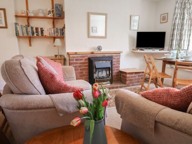 A living room with sofas red pillows a brick fireplace a television and a dining table with chairs at 4 Lymbrook Cottages Lyme Regis