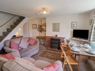A living room with sofas a dining table set with dishes a television and a fireplace at 4 Lymbrook Cottages in Lyme Regis