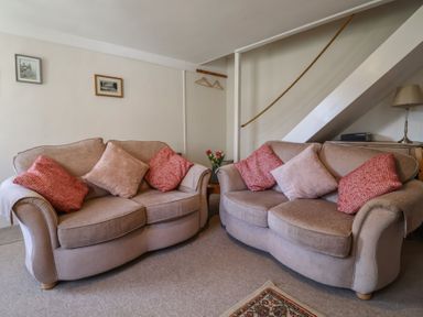 A living room with two beige sofas with red and beige cushions and a small table with flowers at 4 Lymbrook Cottages Lyme Regis