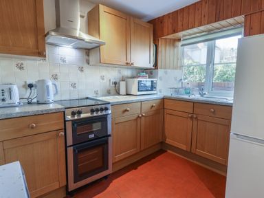 A kitchen with wooden cabinets and drawers a stove a microwave kettle toaster and refrigerator at 4 Lymbrook Cottages Lyme Regis