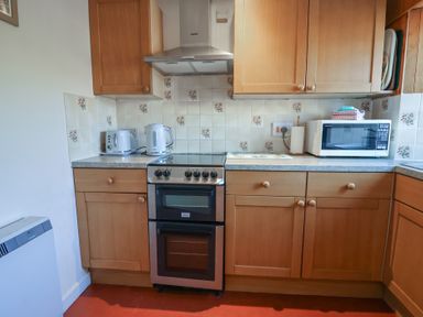 A kitchen with wooden cabinets a stove a microwave a toaster and a kettle at 4 Lymbrook Cottages Lyme Regis