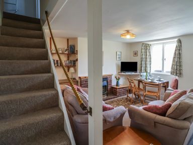 A living room with sofas dining table and chairs by a window and carpeted stairs at 4 Lymbrook Cottages Lyme Regis