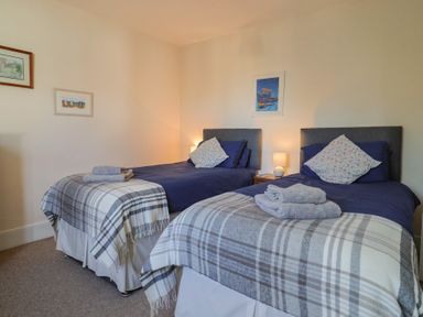 A bedroom with two single beds with plaid throws and pillows at 4 Lymbrook Cottages Lyme Regis