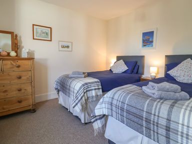 A bedroom with two single beds a wooden dresser and framed pictures on the wall at 4 Lymbrook Cottages Lyme Regis