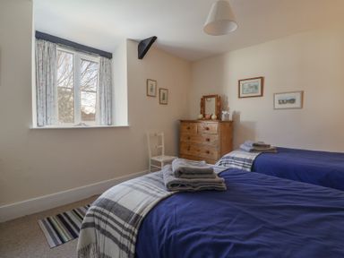 A bedroom with two single beds blue bedding a wooden dresser and a window with curtains at 4 Lymbrook Cottages Lyme Regis