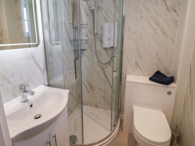 A bathroom with a sink cabinet a corner shower and a toilet with folded towels on the cistern at 4 Lymbrook Cottages in Lyme Regis