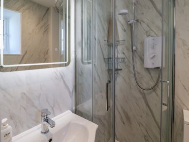 A bathroom with a sink and mirror and a glass-enclosed shower at 4 Lymbrook Cottages Lyme Regis