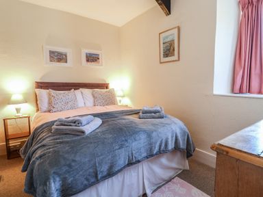 A bedroom with a double bed with towels on the blanket bedside tables with lamps and framed pictures on the walls at 4 Lymbrook Cottages in Lyme Regis