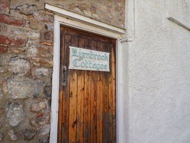 A wooden door with a sign saying Lymbrook Cottages set in a stone and white plaster wall at 4 Lymbrook Cottages in Lyme Regis