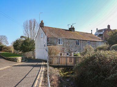 A stone cottage with a sloped roof next to a small wooden bridge over a stream in Lyme Regis