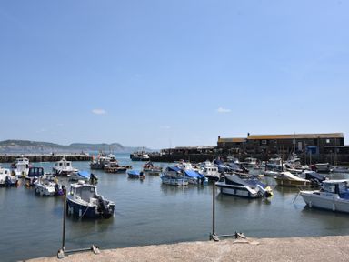 A small harbor with numerous boats docked next to a stone pier with buildings in the background at 4 Lymbrook Cottages Lyme Regis