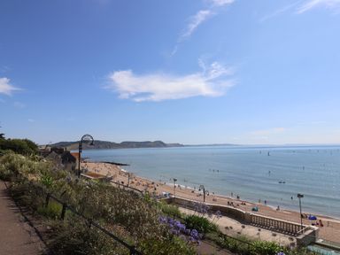 A beach with people on the sand and in the water next to a promenade with plants and lamp posts at 4 Lymbrook Cottages in Lyme Regis