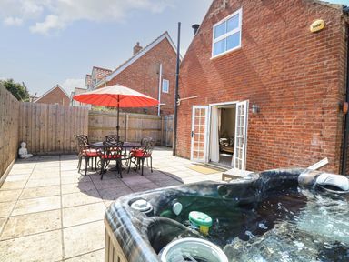 A patio with a hot tub table with umbrella and chairs and open doors leading to a living room at The Old Chapel in Foxley near Bawdeswell