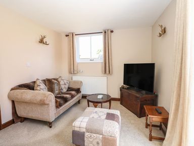 A living room with sofa cushions a patchwork ottoman a television on a wooden chest and a small side table at The Old Chapel in Foxley near Bawdeswell