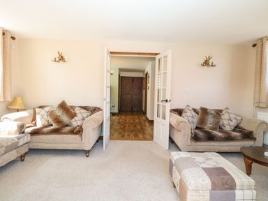 A living room with two beige sofas and an ottoman facing double glass doors at The Old Chapel in Foxley near Bawdeswell