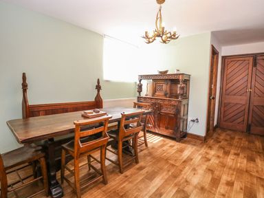 A dining room with wooden table chairs bench cupboard and chandelier at The Old Chapel in Foxley near Bawdeswell
