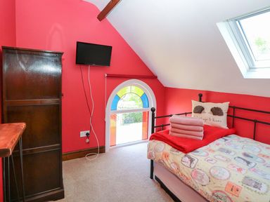 A bedroom with a single bed a quilt a pillow a stack of towels a wooden wardrobe a wall-mounted television and a window at The Old Chapel in Foxley near Bawdeswell
