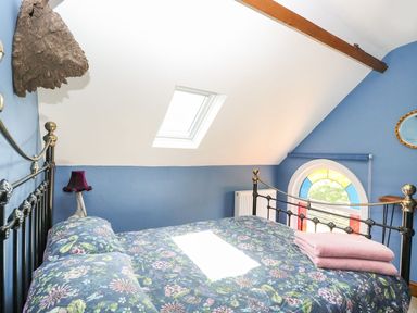 A bedroom with a bed that has floral bedding a skylight window and a round stained glass window at The Old Chapel in Foxley near Bawdeswell