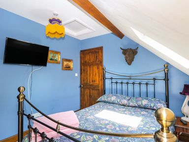 A bedroom with a bed with floral bedding a wooden door a wall-mounted television and framed pictures at The Old Chapel in Foxley near Bawdeswell