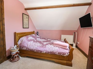 A bedroom with a wooden bed pink floral bedding a television mounted on the wall and a fan at The Old Chapel in Foxley near Bawdeswell