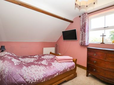 A bedroom with a wooden bed covered with floral bedding a chest of drawers and a wall-mounted television at The Old Chapel in Foxley near Bawdeswell