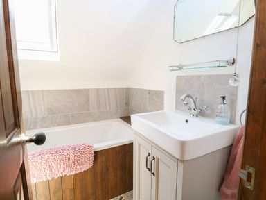 A bathroom with a bathtub with wood paneling a white sink cabinet a wall-mounted mirror and a pink towel at The Old Chapel in Foxley near Bawdeswell